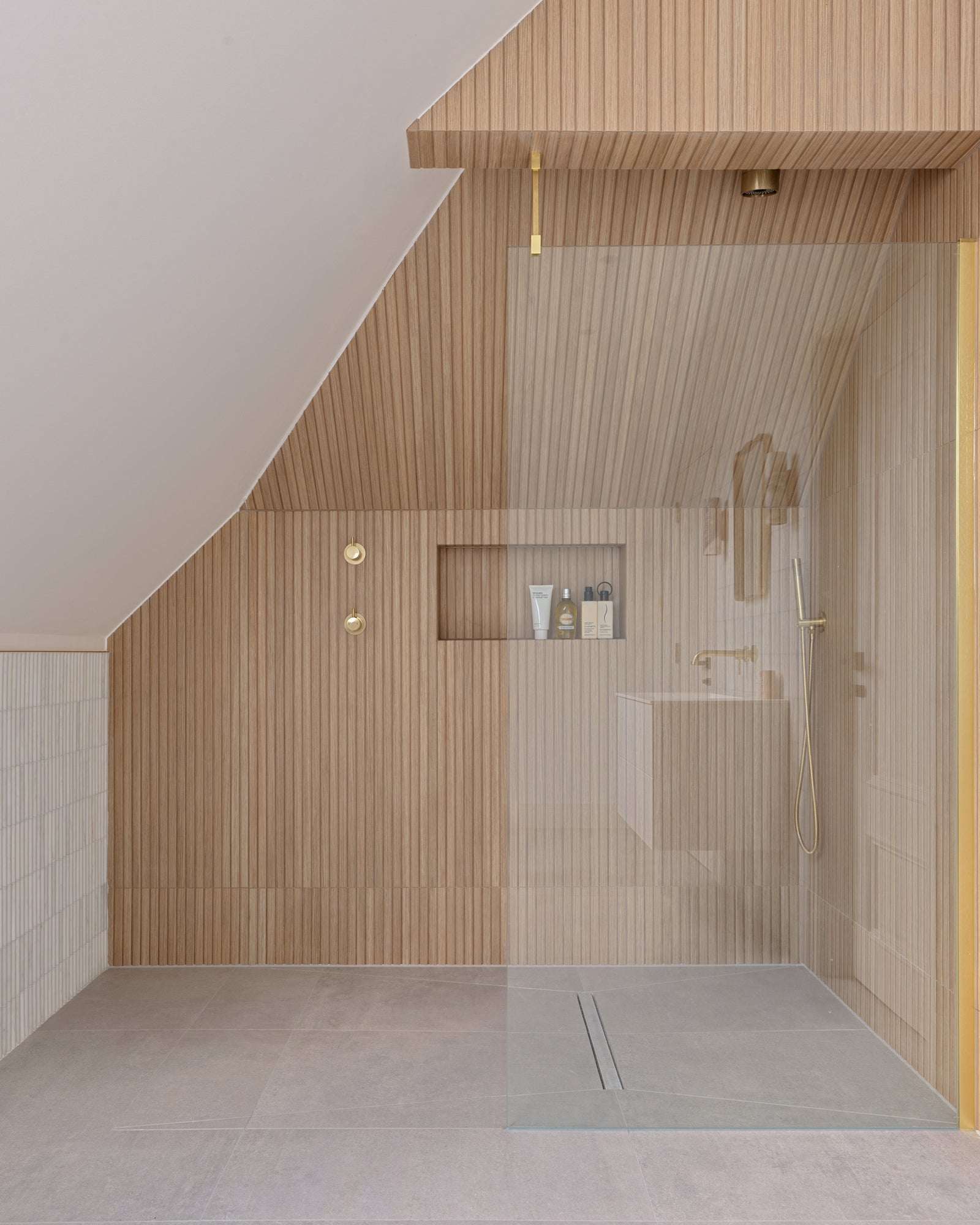 Louvre Porcelain Perla fluted tile in a loft bathroom, running as a dado beside a walk-in shower lined in warm timber-effect fluting with brushed brass fittings and a recessed niche