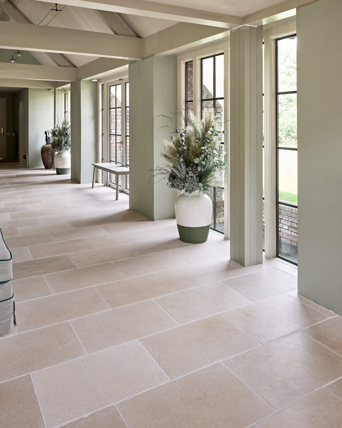 Mallory Limestone Tumbled Finish laid through a sage green garden room corridor with steel casement doors and tall planted urns