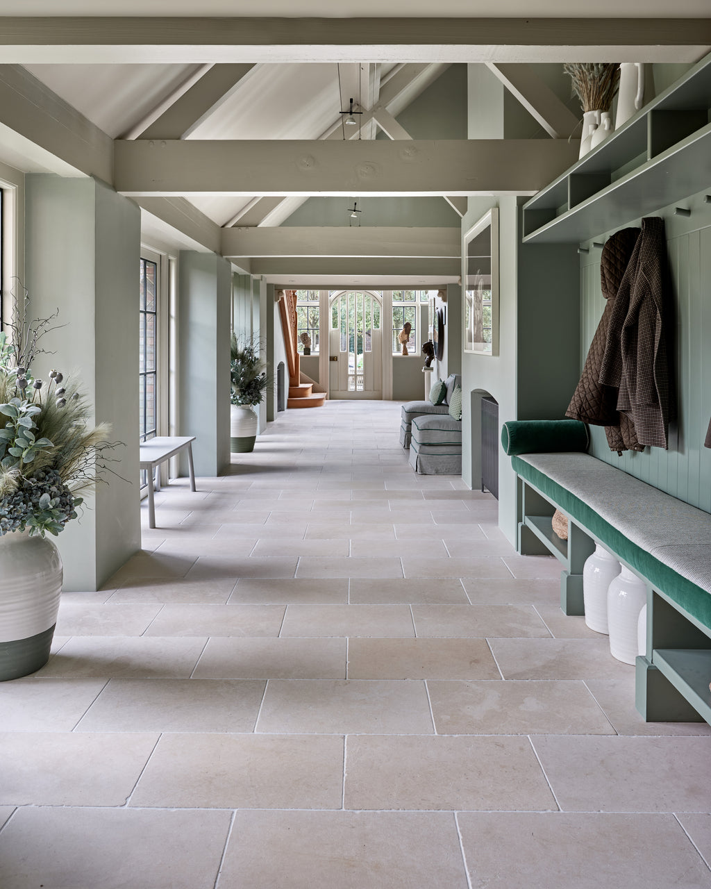 Mallory Limestone Tumbled Finish running the length of a green panelled boot room with a velvet bench seat and coat hooks