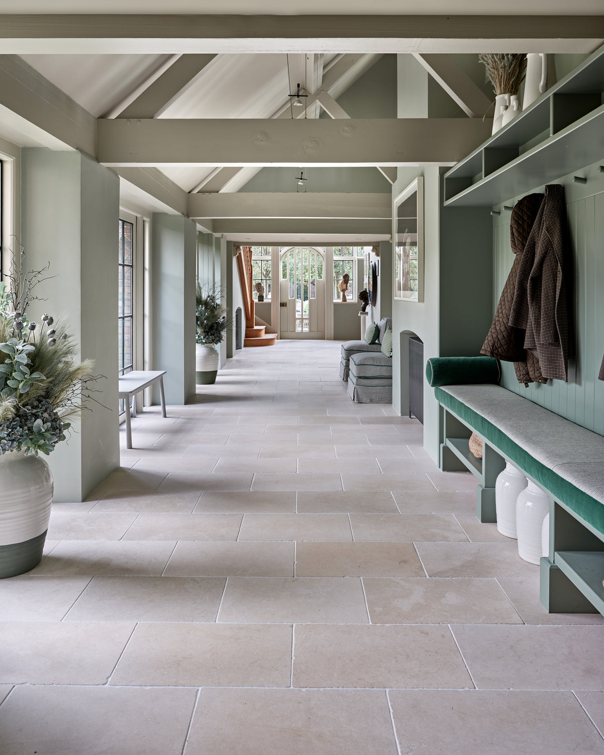 Mallory Limestone Tumbled Finish running the length of a green panelled boot room with a velvet bench seat and coat hooks