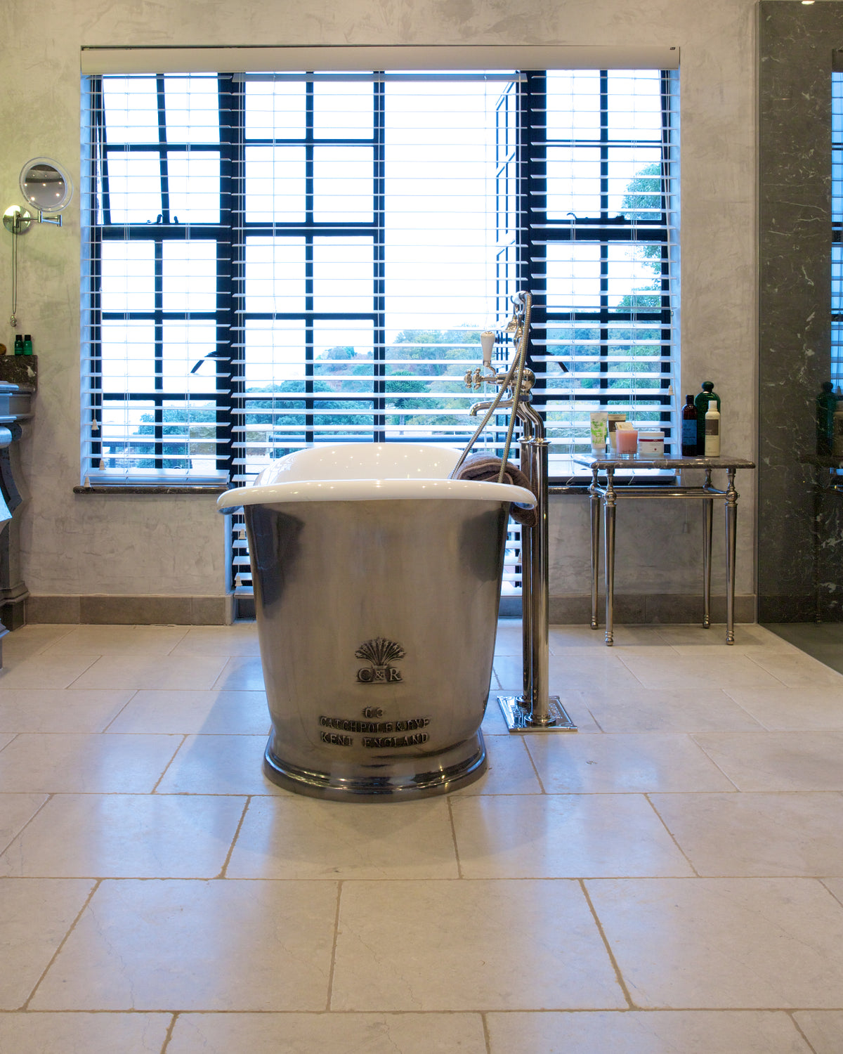 Mallory Limestone Tumbled Finish across a bathroom floor beneath a polished nickel roll top bath and shuttered window