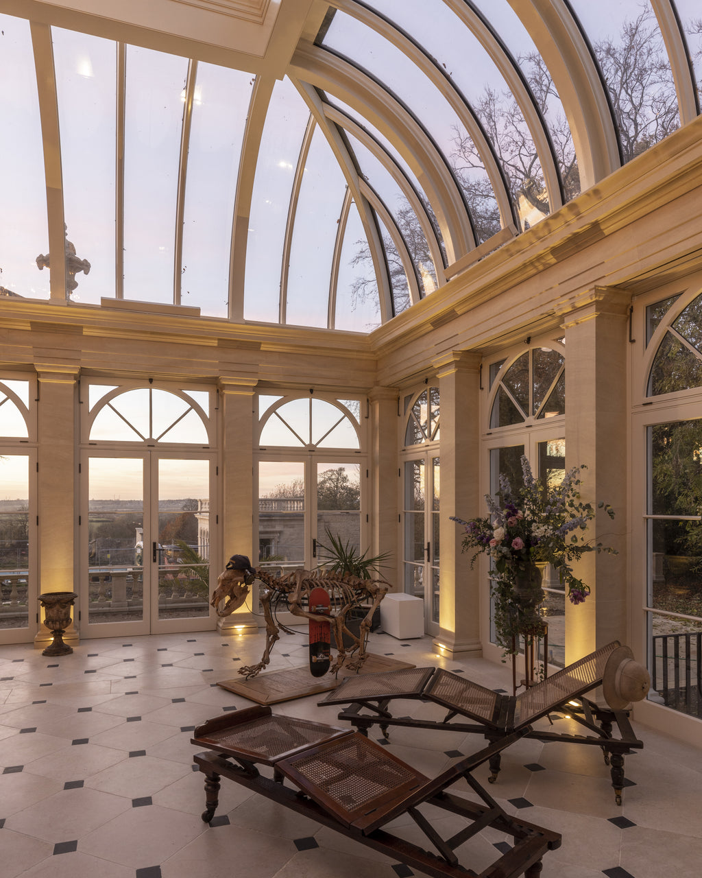 Mallory Limestone Tumbled Finish with dark cabochon insets across an orangery floor beneath a glazed vaulted roof at dusk
