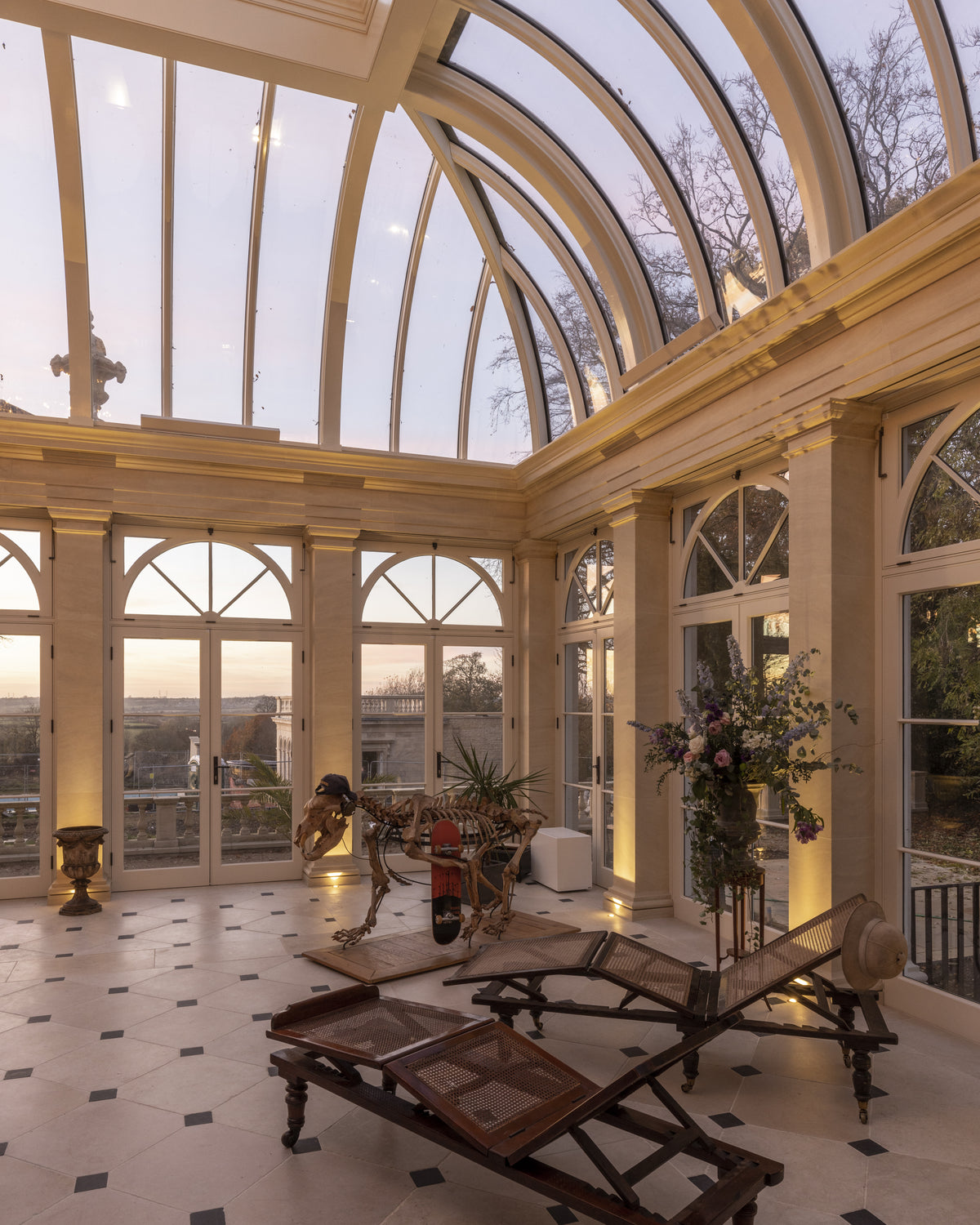 Mallory Limestone Tumbled Finish with dark cabochon insets across an orangery floor beneath a glazed vaulted roof at dusk