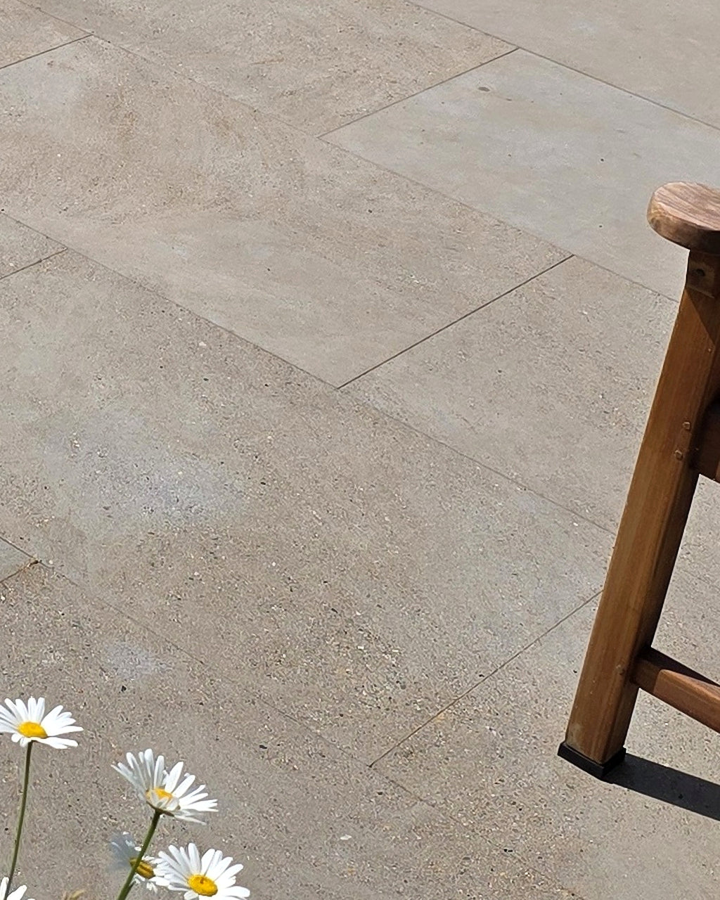 Matravers Sandstone Sawn paving in 60x90cm slabs, a sunlit close-up of the fine sawn surface beside a wooden stool and a clump of ox-eye daisies