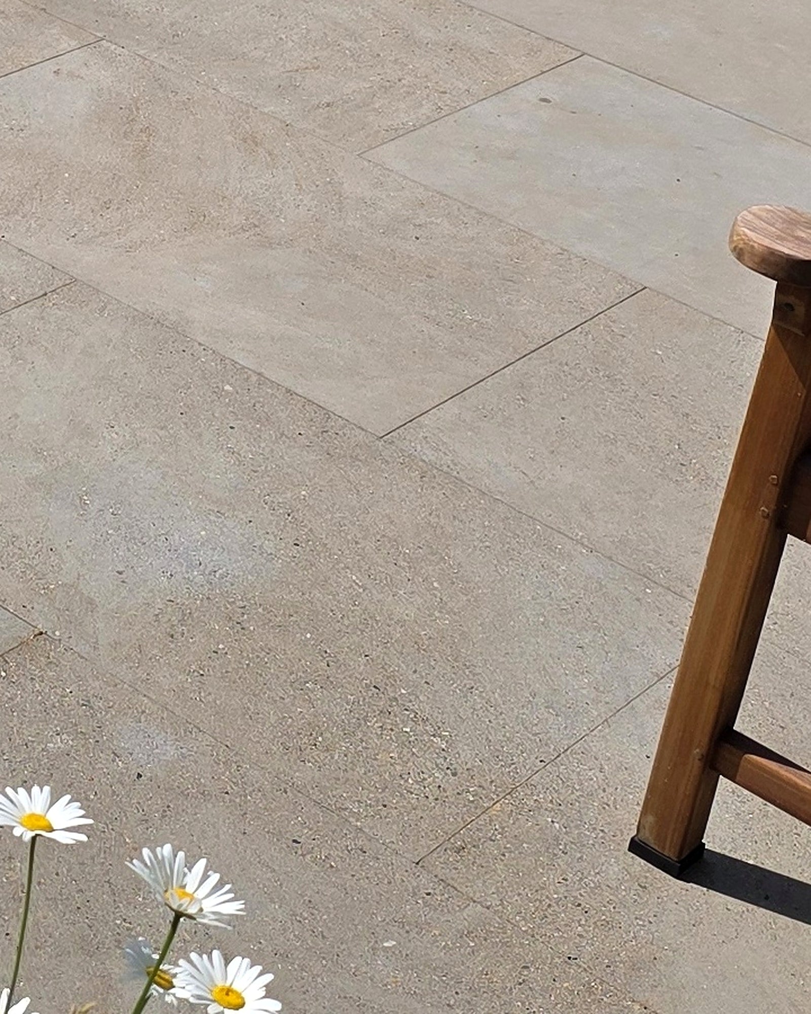 Matravers Sandstone Sawn paving in 60x90cm slabs, a sunlit close-up of the fine sawn surface beside a wooden stool and a clump of ox-eye daisies