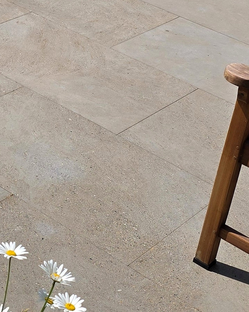 Matravers Sandstone Sawn paving in 60x90cm slabs, a sunlit close-up of the fine sawn surface beside a wooden stool and a clump of ox-eye daisies