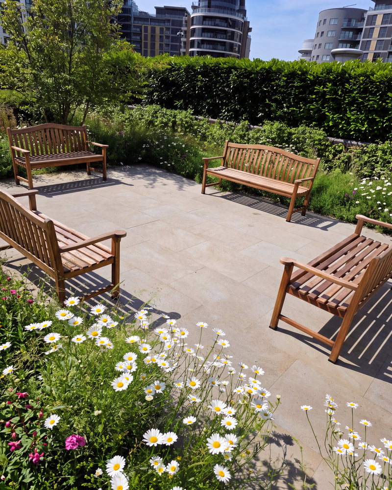 Matravers Sandstone Sawn paving forming a garden seating terrace with four teak benches, wildflower planting and a clipped hedge, city apartment buildings beyond