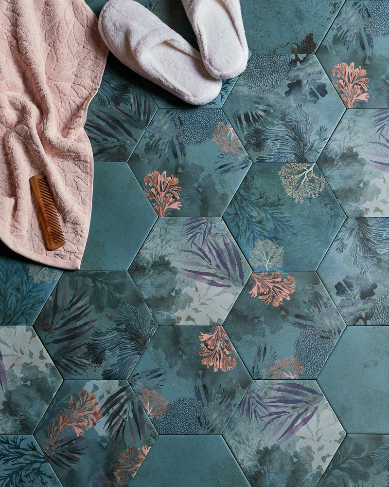 Mermaid's Garden Porcelain hexagons laid as a bathroom floor, seen from above with a pink waffle towel, slippers and wooden comb across the seaweed and coral pattern