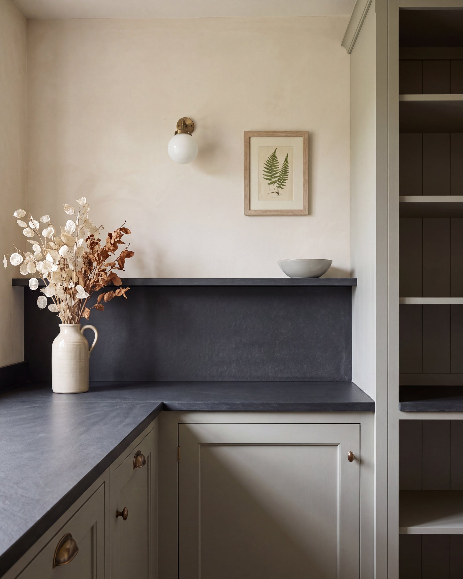 Metropolitan Slate Riven Slab as a pantry worktop, upstand and shelf, against limewashed walls and pale green shaker cabinetry with aged brass handles