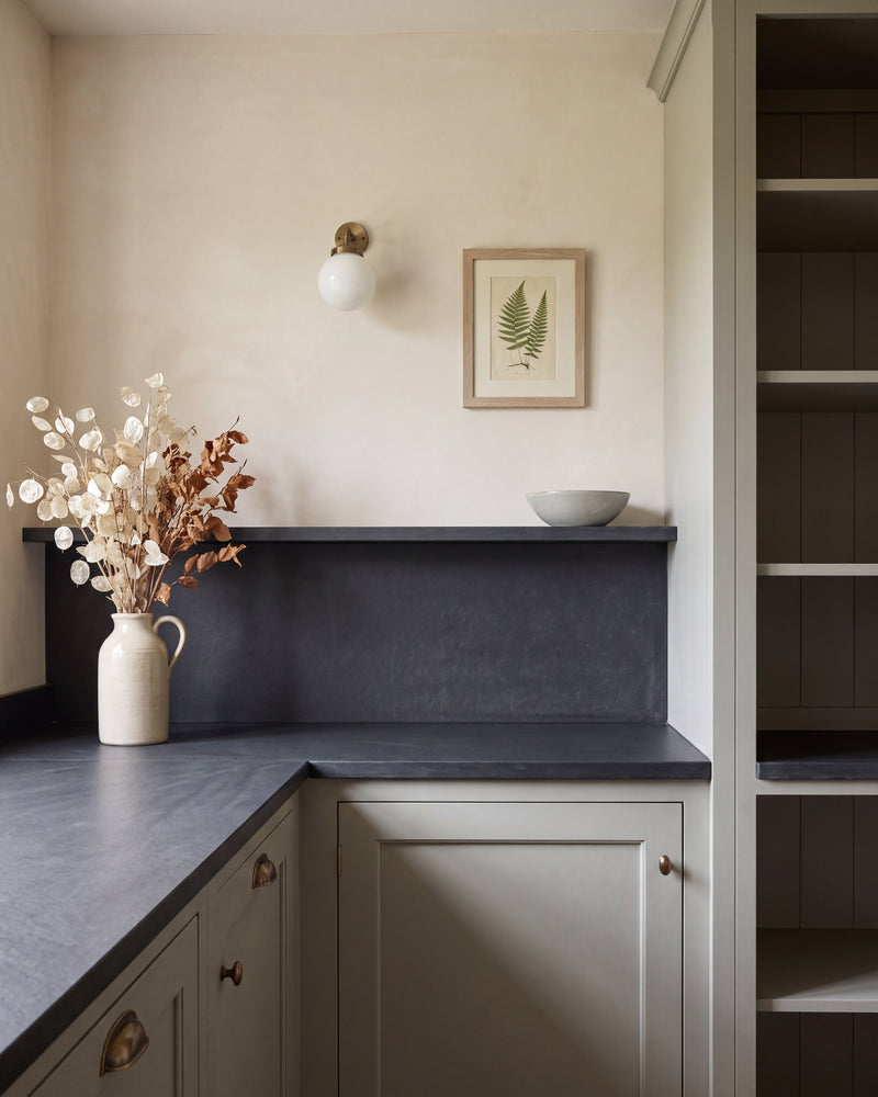 Metropolitan Slate Riven Slab as a pantry worktop, upstand and shelf, against limewashed walls and pale green shaker cabinetry with aged brass handles