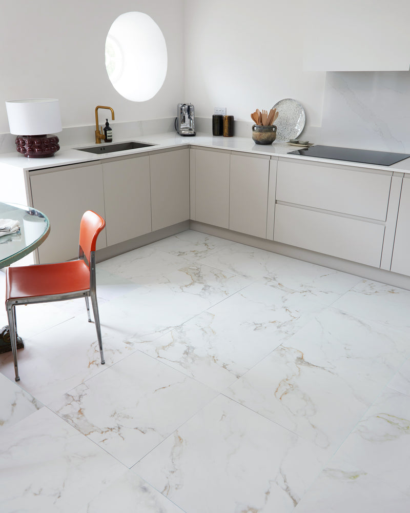 Muscat Porcelain Satin floor tiles laid large format in a pale contemporary kitchen with a round window and an orange leather chair