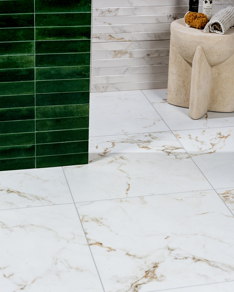 Muscat Porcelain Satin floor and wall tiles meeting a deep green glazed brick wall, with a travertine stool and rolled towels