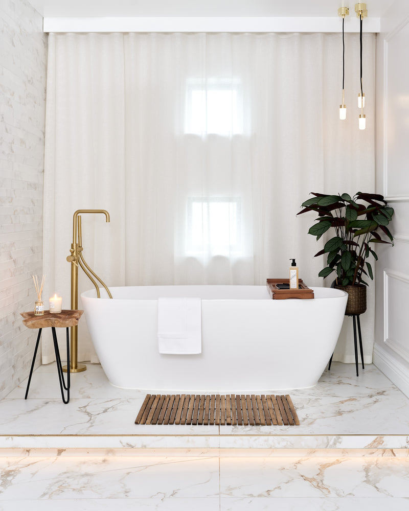 Muscat Porcelain Satin marble effect tiles across a bright bathroom floor and step beneath a freestanding bath with brass pendant lights