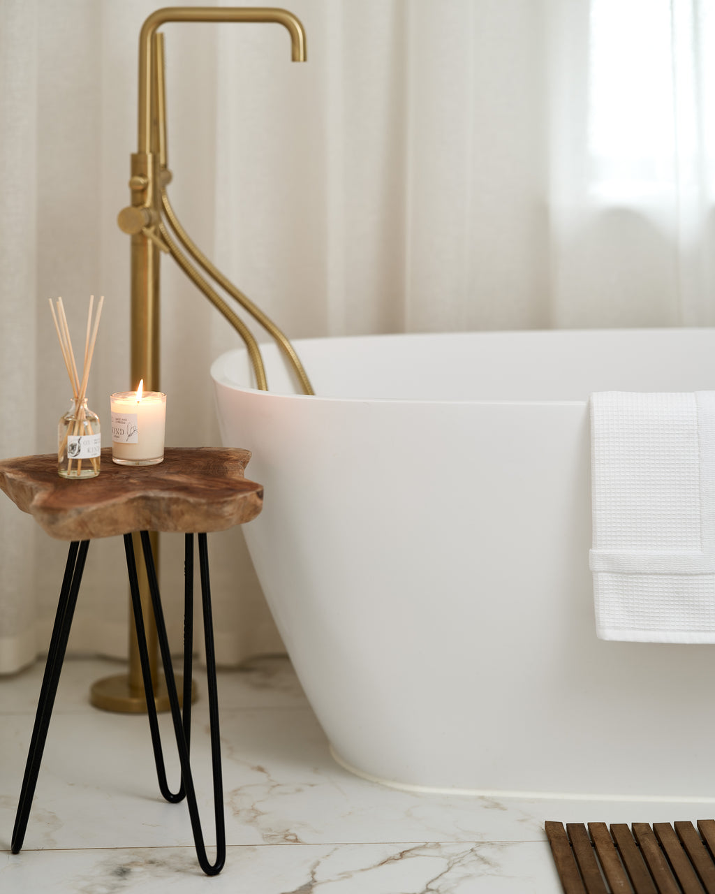 Close up of Muscat Porcelain Satin flooring with its warm gold veining beside a freestanding bath, brass floor standing tap and a rustic wooden side table