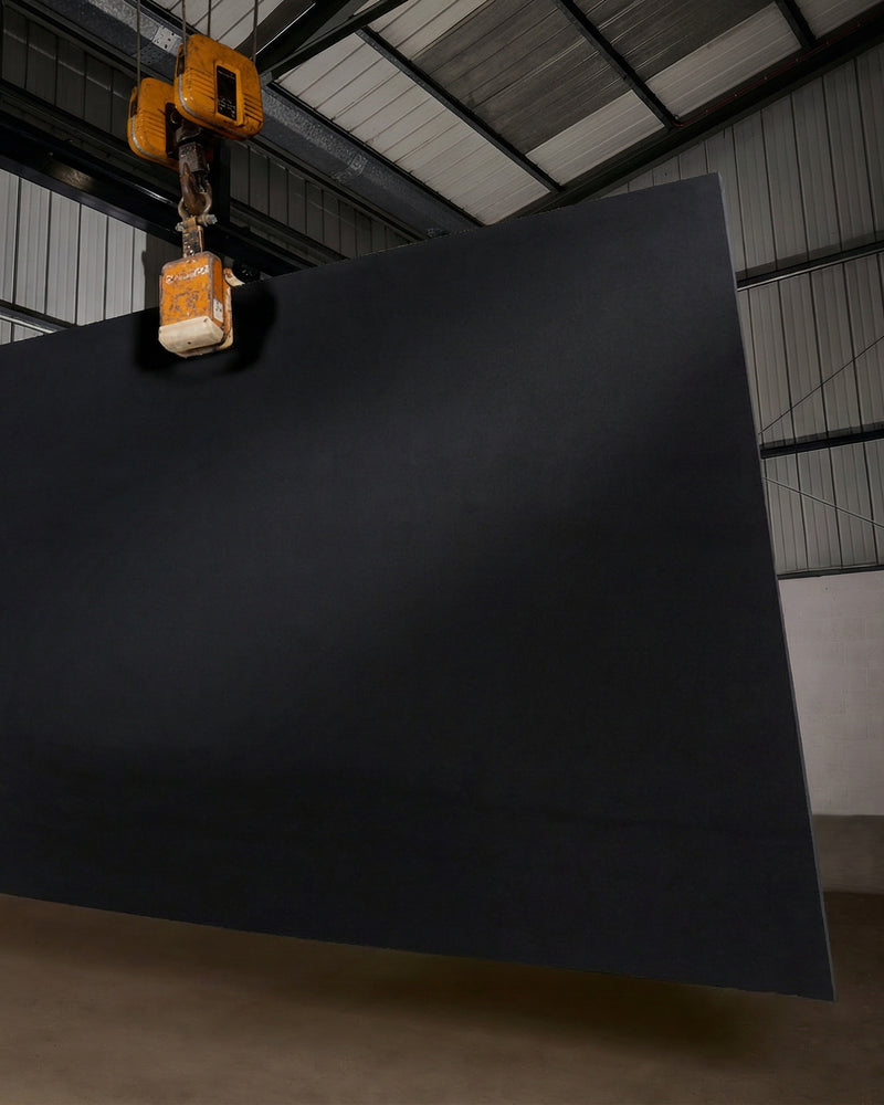 A full Nero Slate Honed Slab suspended from a warehouse crane hoist, showing the scale and deep matt charcoal of a single uncut sheet