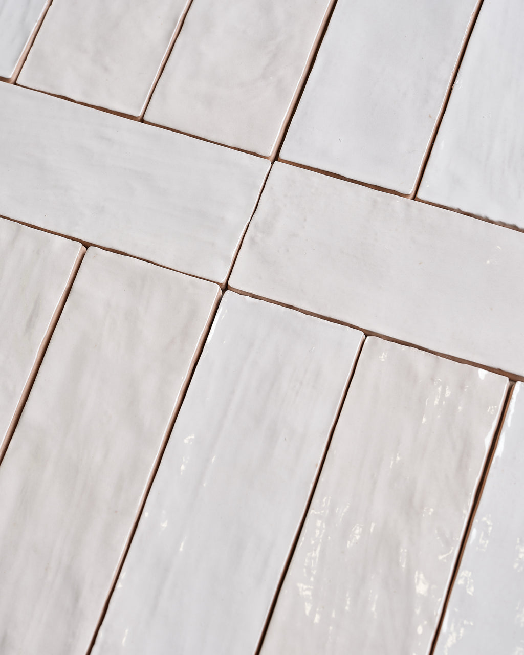 Oasis Ceramic White Gloss brick format tiles laid out loose, showing the undulating hand-glazed surface and the soft white variation across the batch