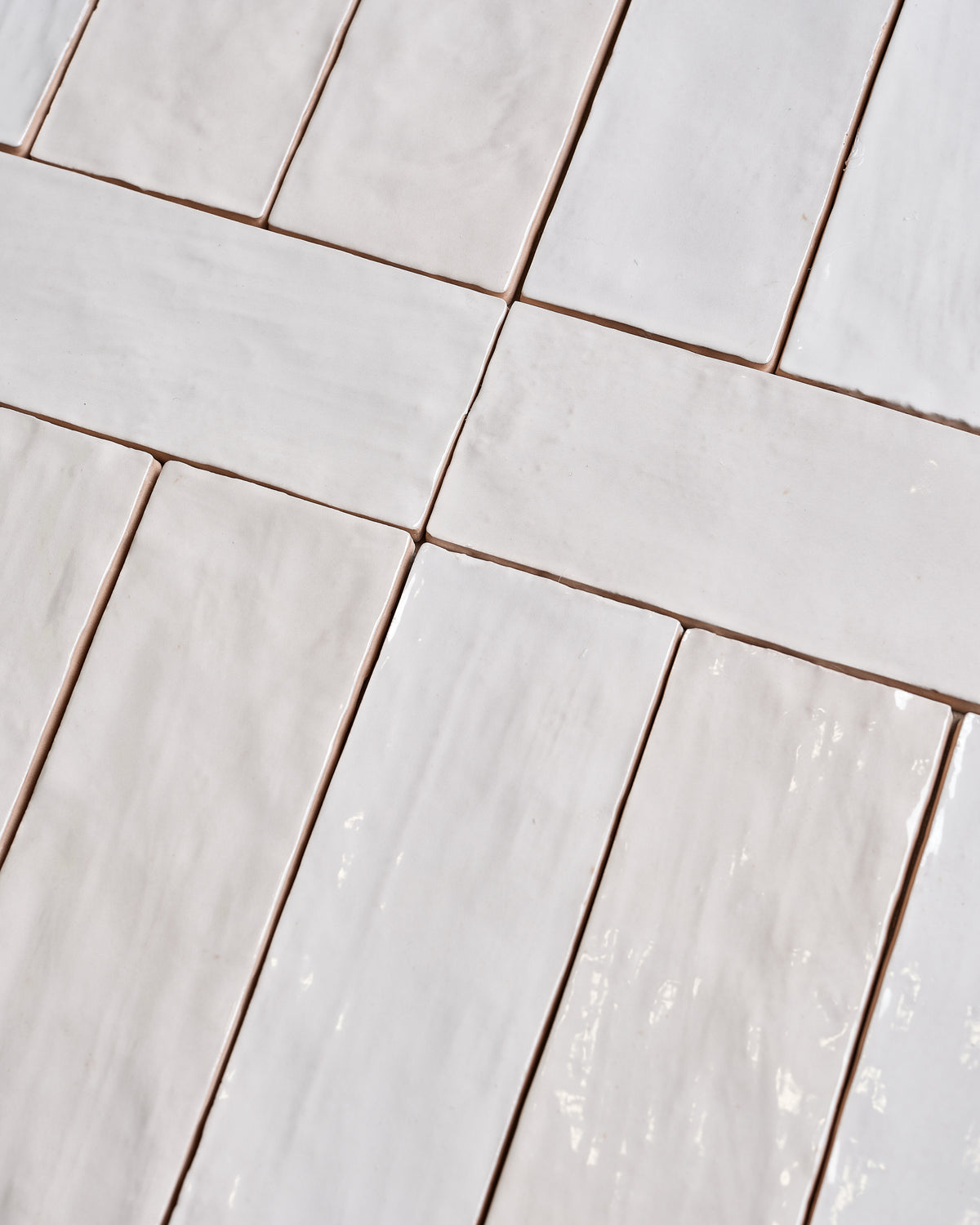 Oasis Ceramic White Gloss brick format tiles laid out loose, showing the undulating hand-glazed surface and the soft white variation across the batch