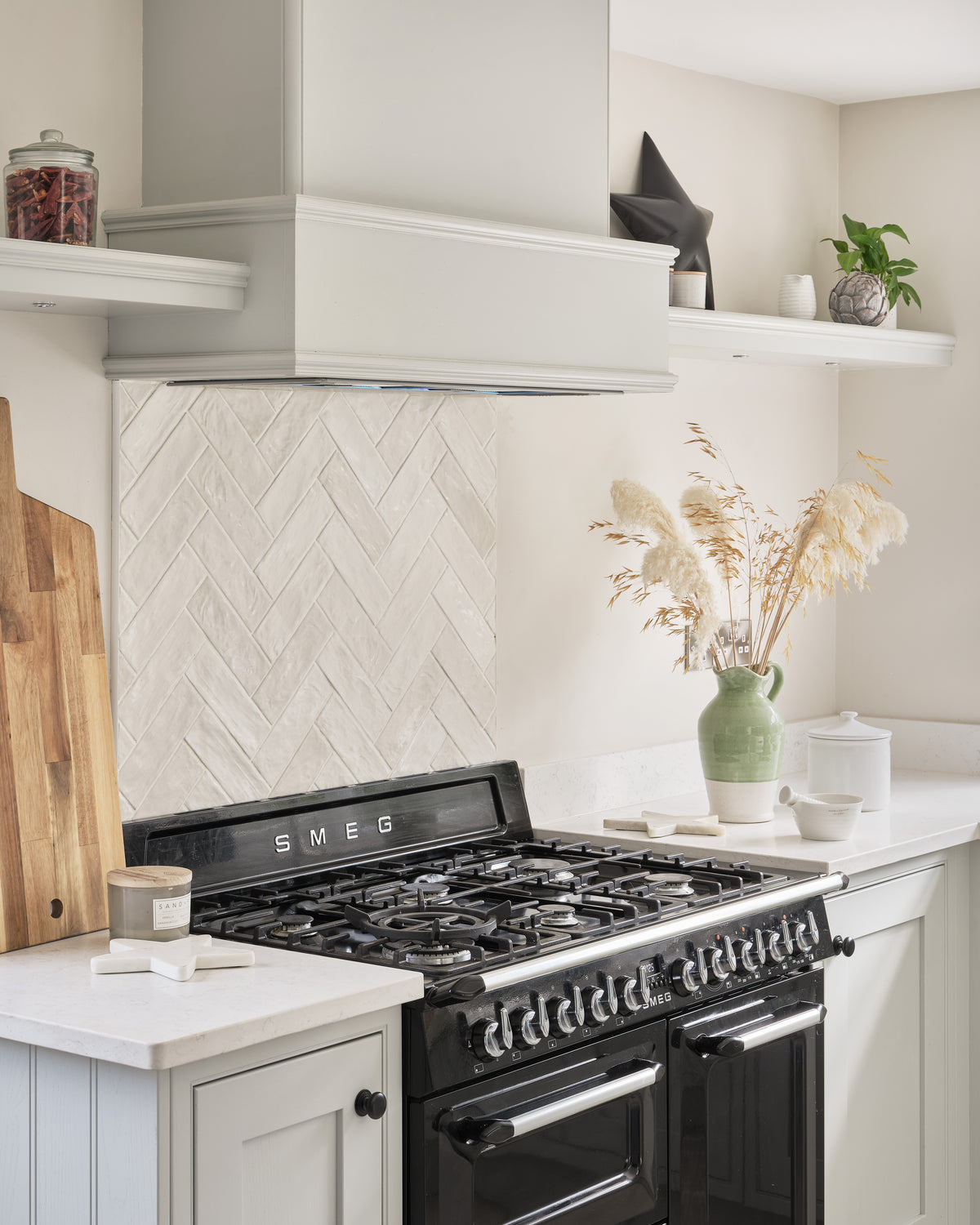 Oasis Ceramic White Gloss laid in a herringbone splashback behind a black SMEG range cooker, framed by painted shelves and a boarded extractor hood