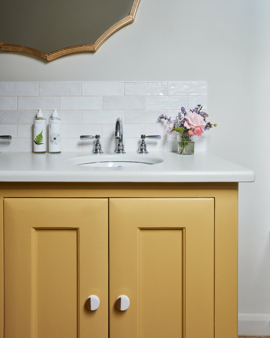 Oasis Ceramic White Gloss as a slim splashback above a mustard yellow vanity unit in a cloakroom, beneath a gold scalloped mirror