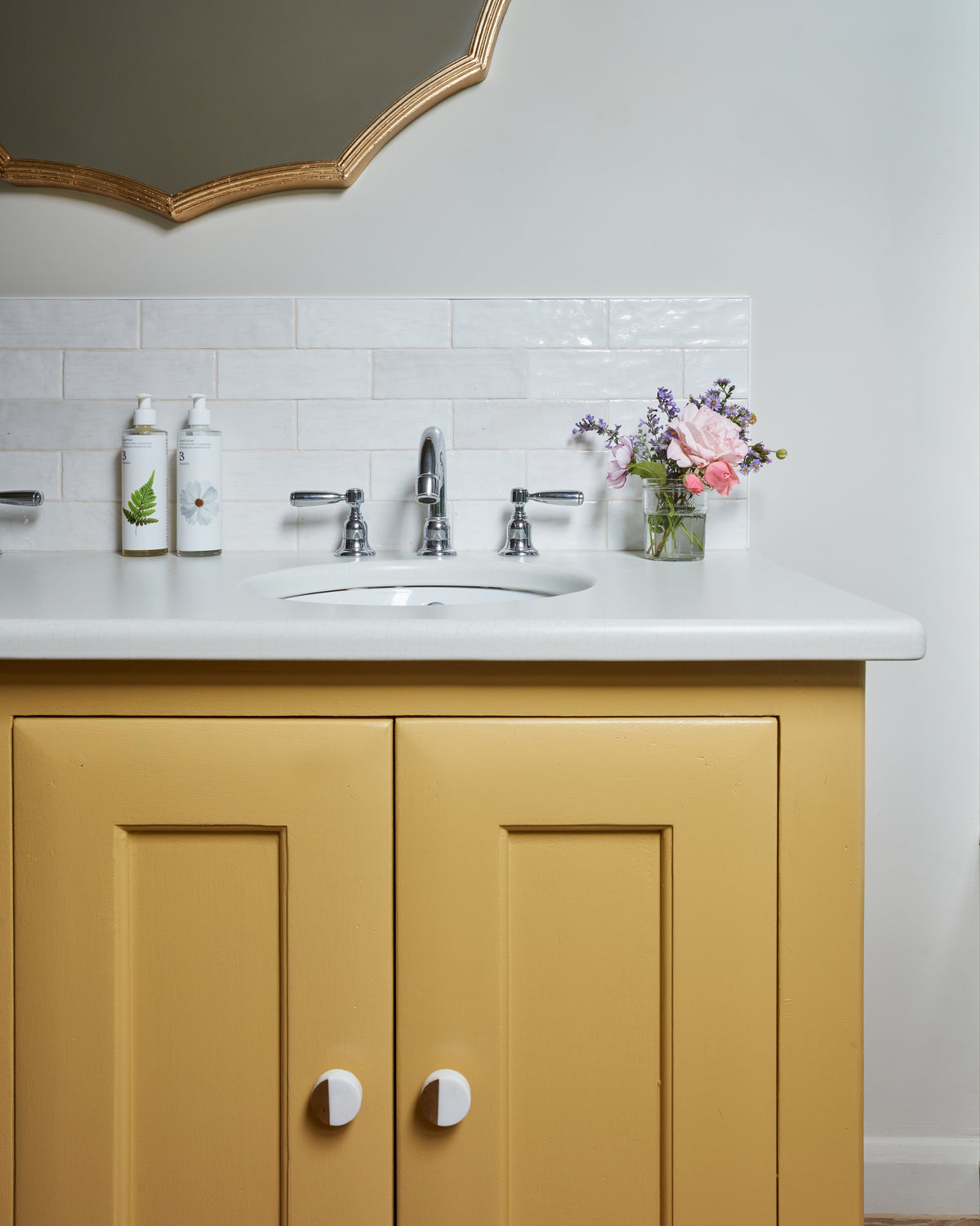 Oasis Ceramic White Gloss as a slim splashback above a mustard yellow vanity unit in a cloakroom, beneath a gold scalloped mirror