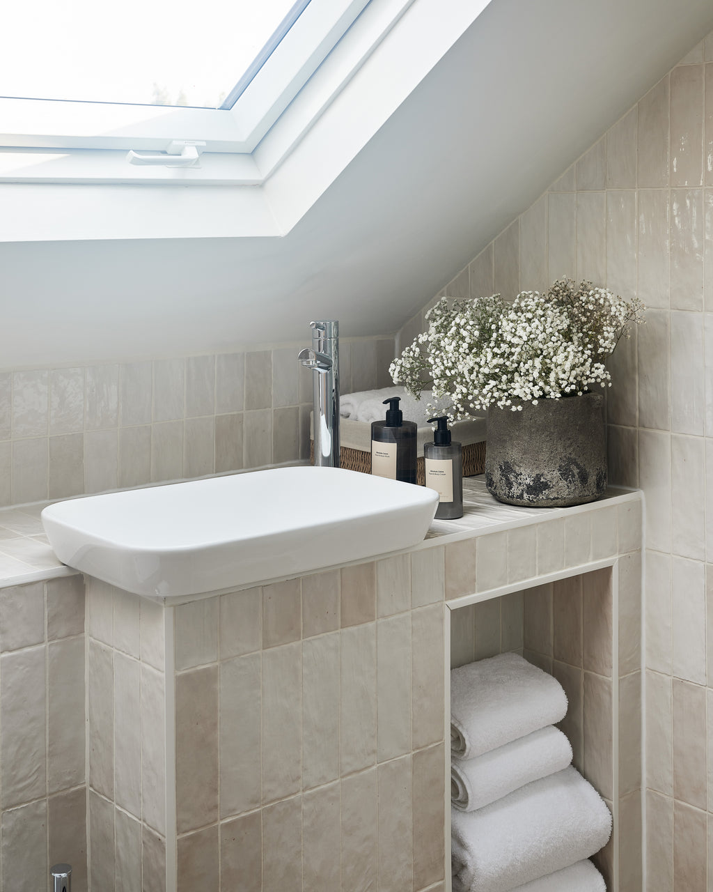 Oasis Ceramic White Gloss tiling the vanity and sloping wall of a loft bathroom beneath a skylight, with towels stacked in an open alcove