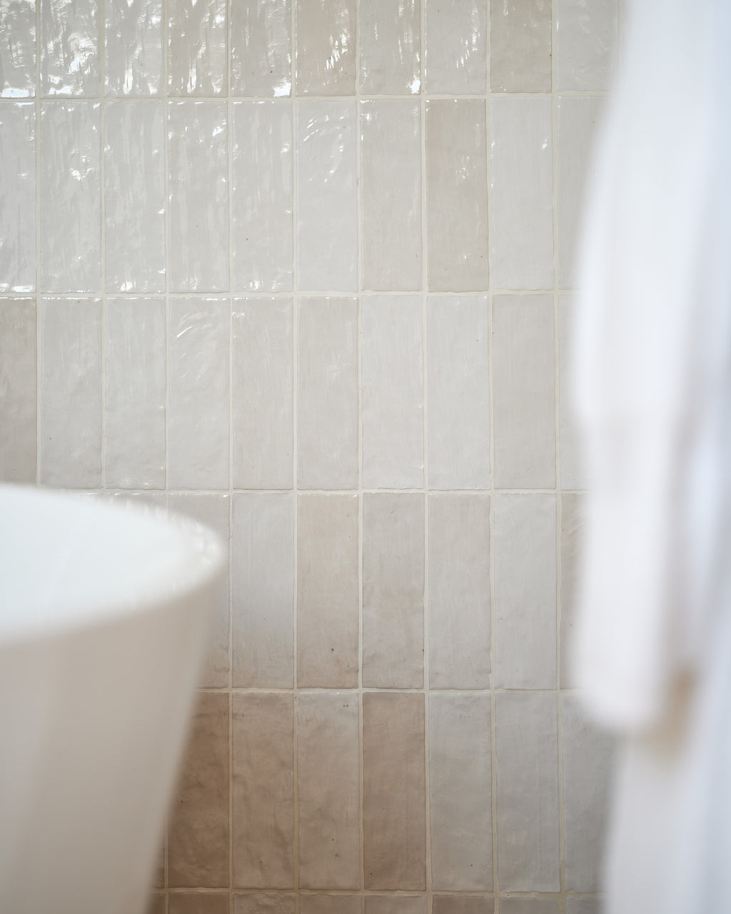 Oasis Ceramic White Gloss stacked vertically beside a freestanding bath, showing the tonal variation and glaze movement across the wall