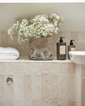 Oasis Ceramic White Gloss tiling a bath surround and shelf, styled with gypsophila in a stone pot, folded towels and hand wash