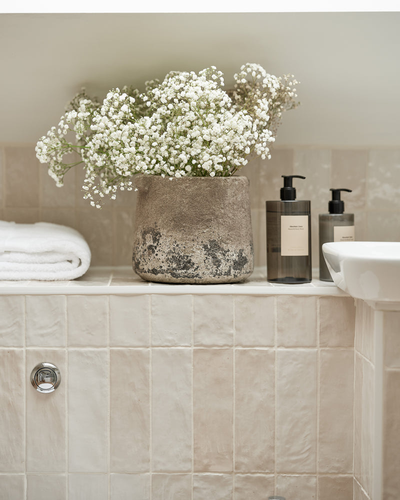 Oasis Ceramic White Gloss tiling a bath surround and shelf, styled with gypsophila in a stone pot, folded towels and hand wash