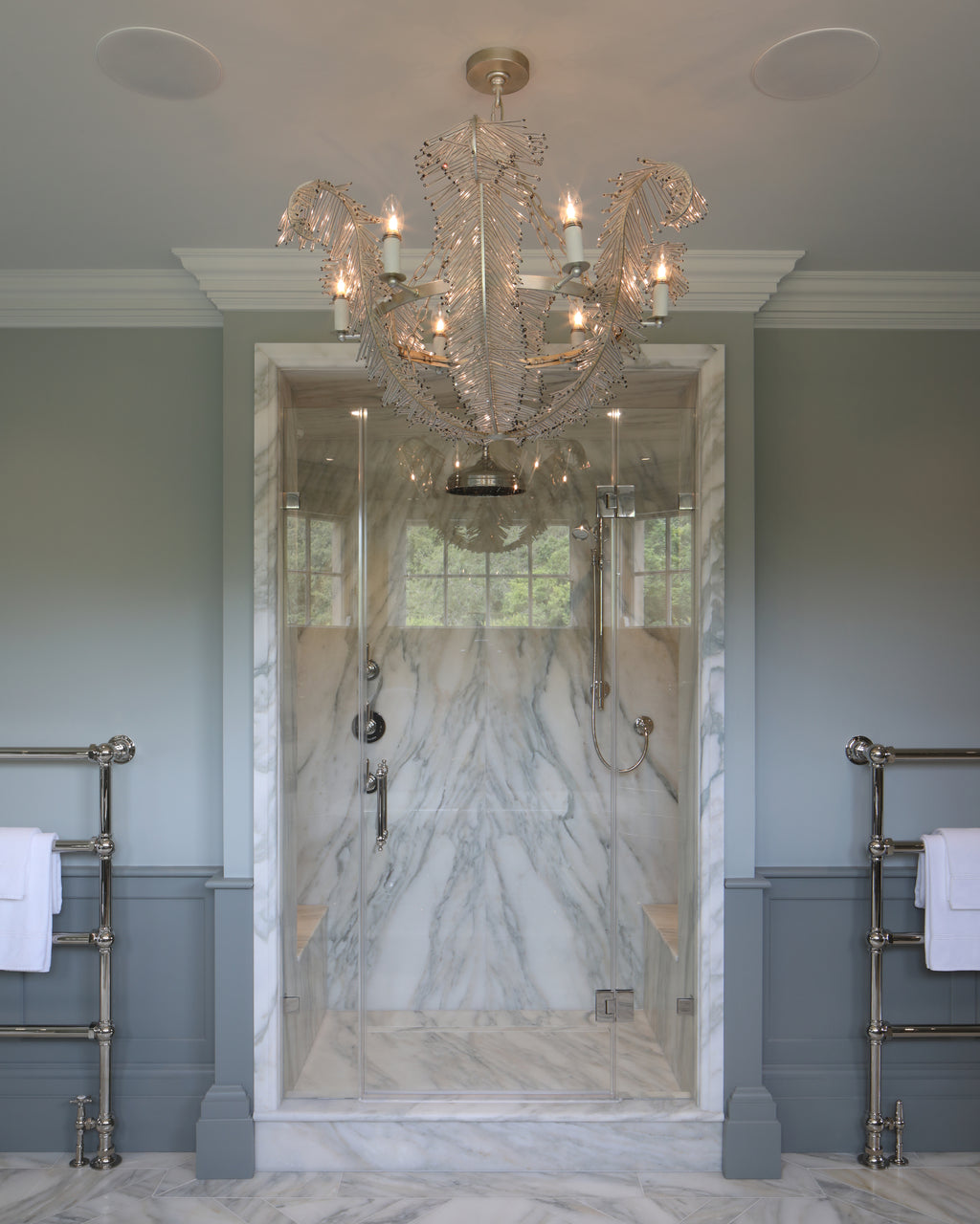 Palazzo Oro Marble Honed Slab lining a walk-in shower enclosure and running across the floor of a pale green panelled bathroom, with a feather chandelier overhead