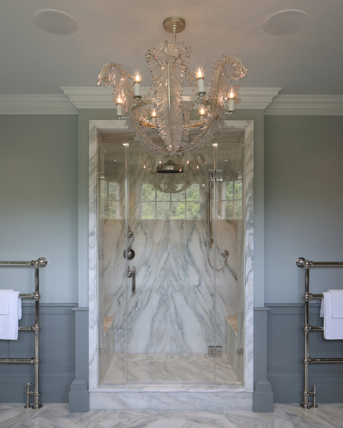 Palazzo Oro Marble Honed Slab lining a walk-in shower enclosure and running across the floor of a pale green panelled bathroom, with a feather chandelier overhead