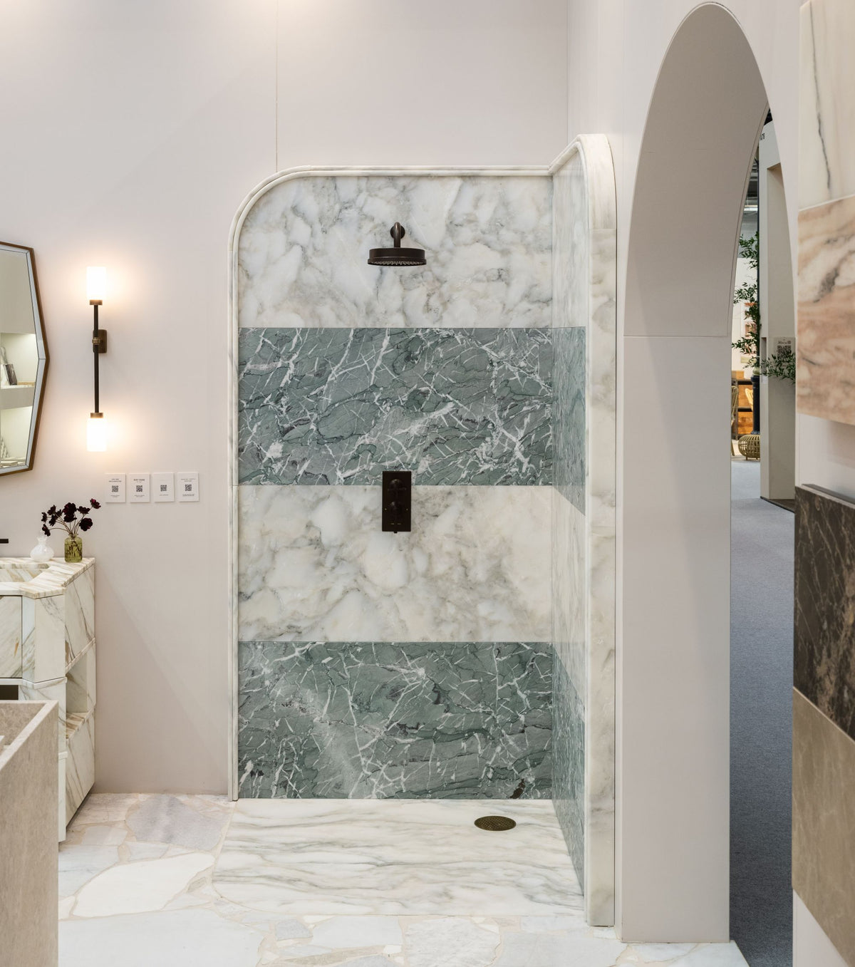 Palazzo Oro Marble Honed Slab lining a curved walk-in shower with banded green marble and bronze fittings, shown on a Ca'Pietra exhibition stand