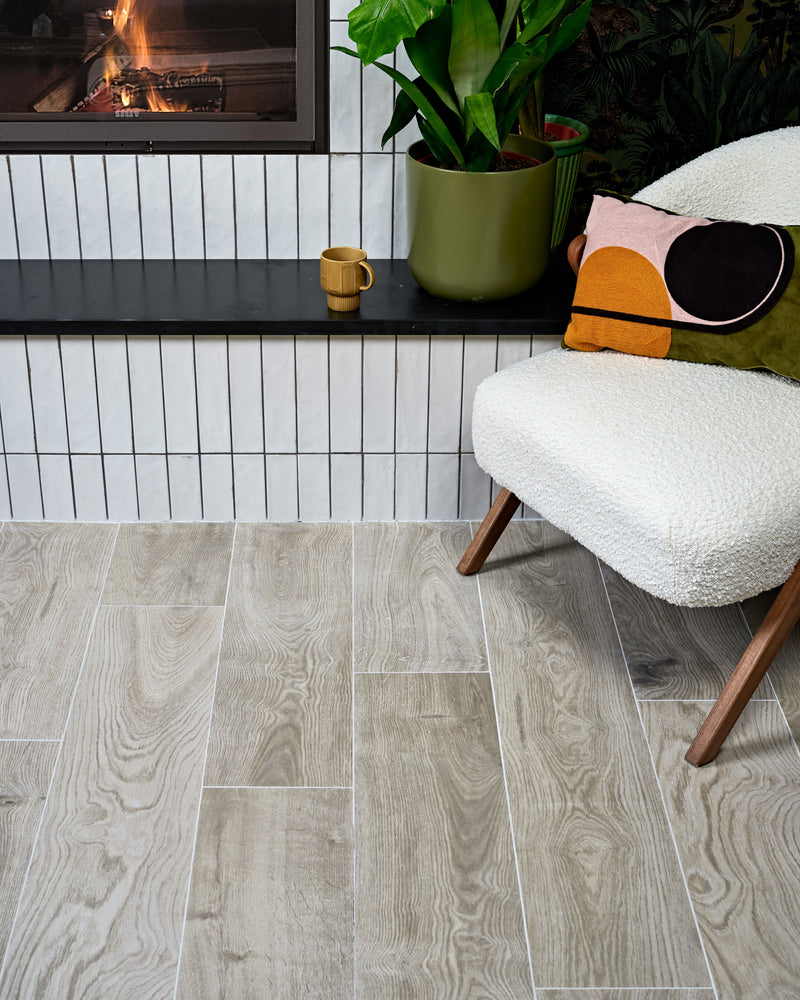 Parterre Porcelain Plank across a living room floor beside a lit fireplace clad in Foundry Leadenhall White, with a boucle chair and jungle-print wallpaper