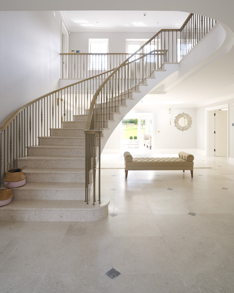 Piccadilly Limestone Honed Finish laid with small grey inset squares across a double-height entrance hall with a curved stone staircase