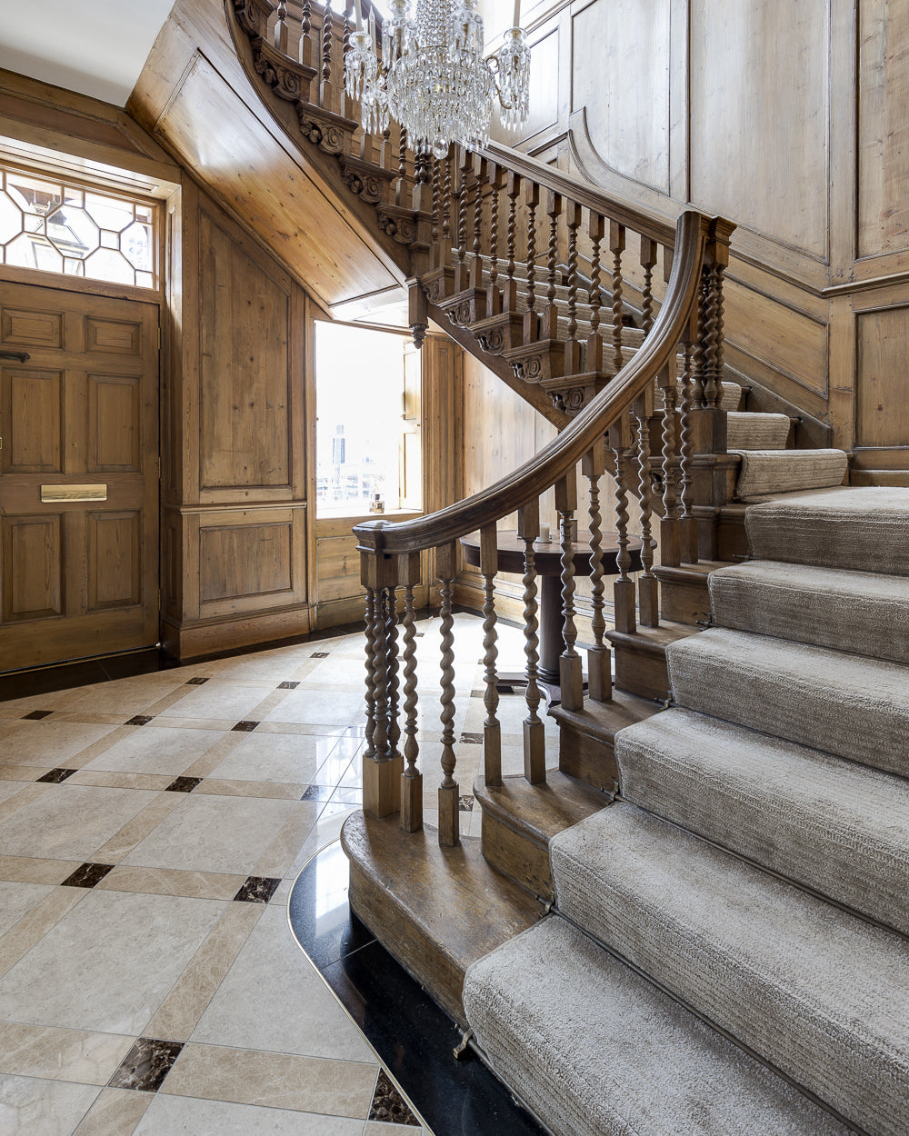 Piccadilly Limestone Honed Finish with a black border framing the foot of a carved barley-twist staircase