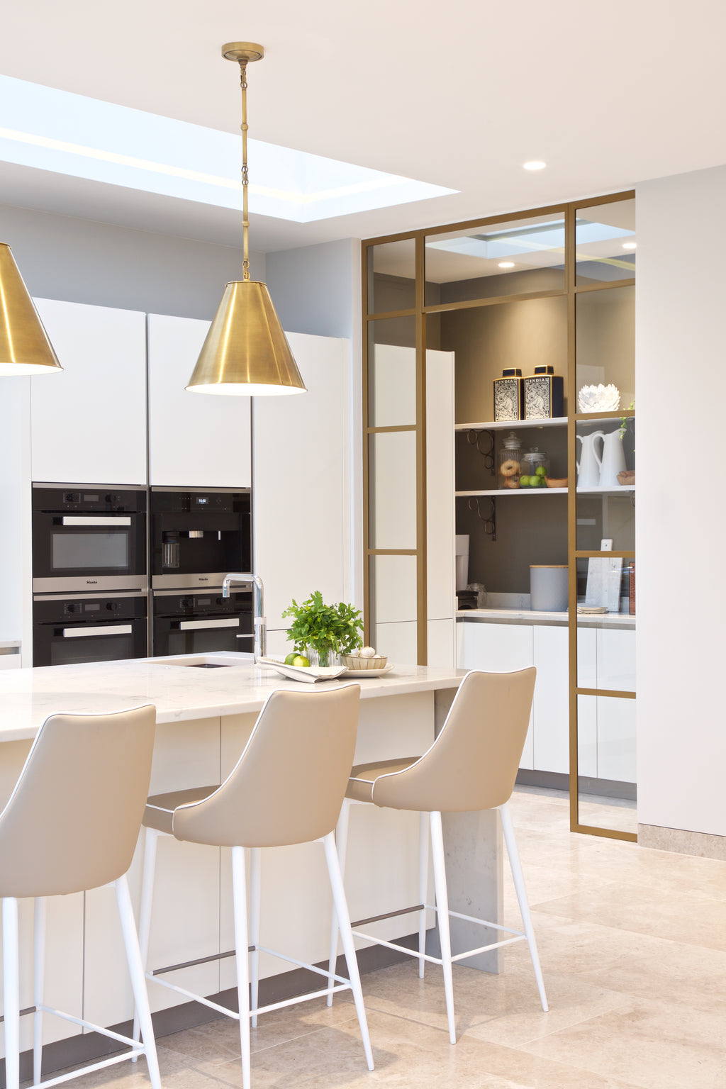 Piccadilly Limestone Honed Finish laid through an open plan kitchen with white handleless cabinetry, brass pendants and a brass framed pantry screen