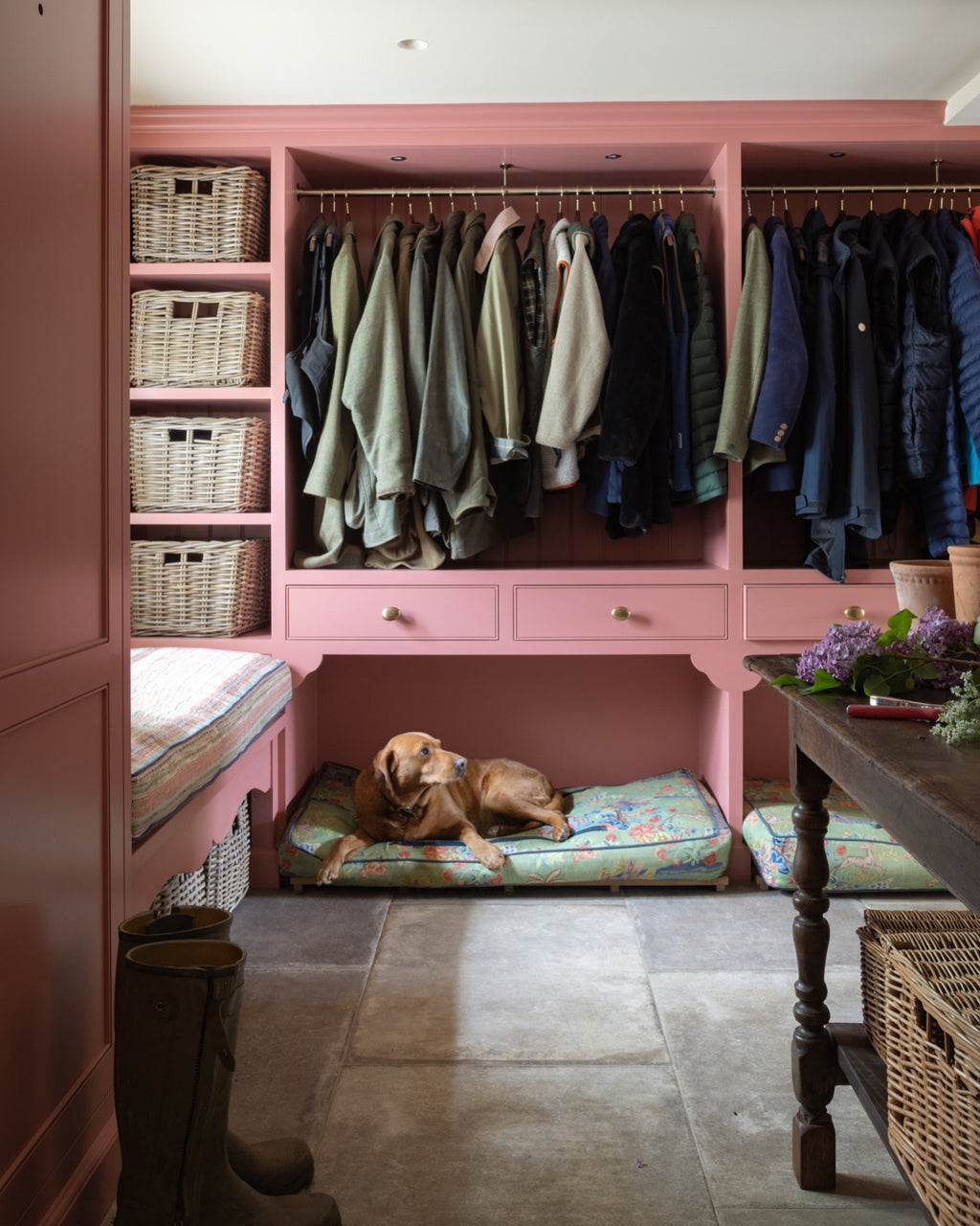 Provence Porcelain Cenere flagstones across a boot room floor, with pink painted joinery, hanging coats, wicker baskets and a labrador asleep on a floral cushion
