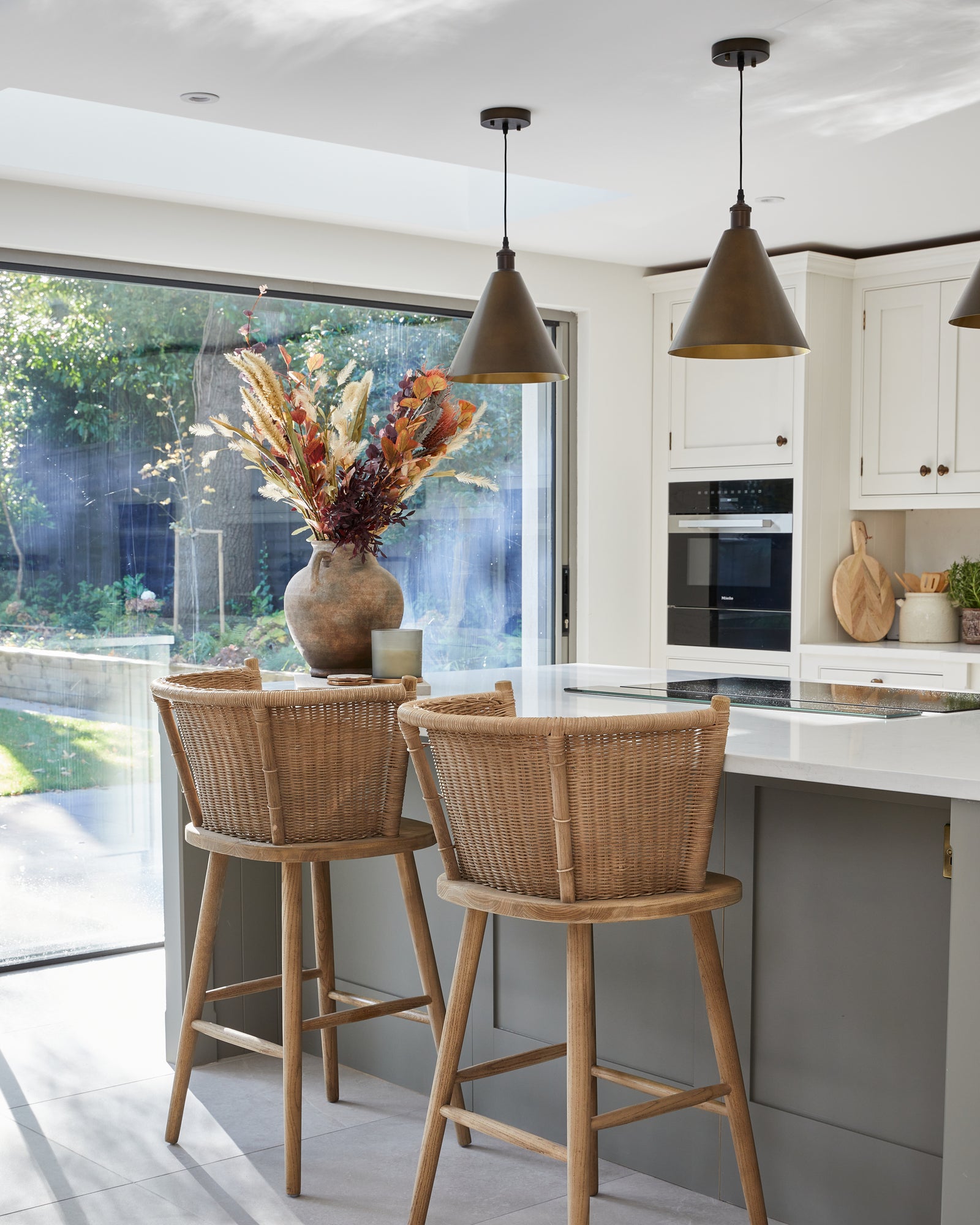Riverside Porcelain Perla large-format floor tiles running through a shaker kitchen to open sliding doors, with two rattan bar stools at a green island