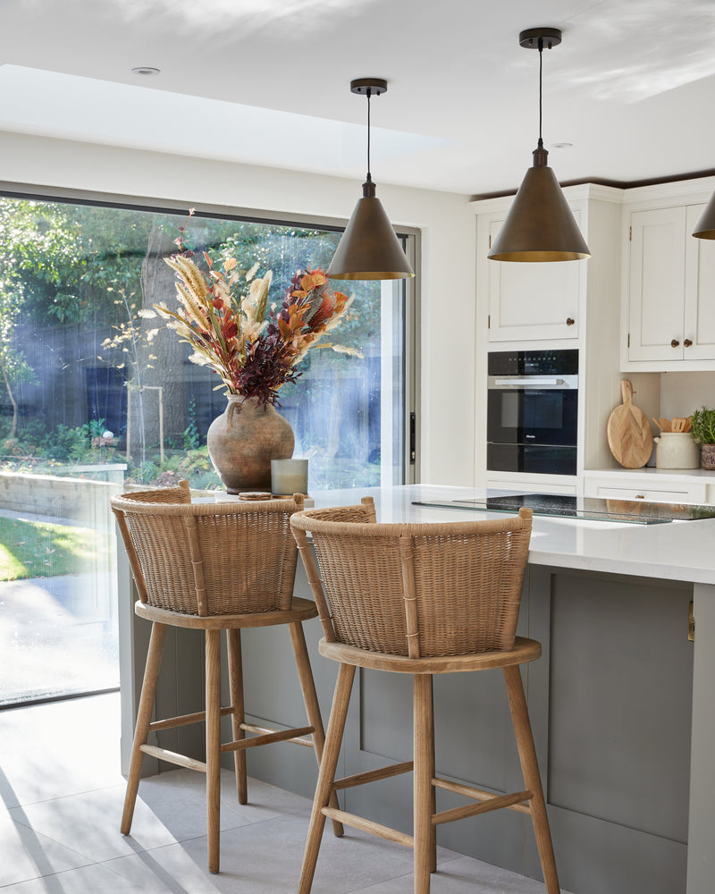 Riverside Porcelain Perla large-format floor tiles running through a shaker kitchen to open sliding doors, with two rattan bar stools at a green island