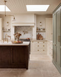 Riviera Limestone Tumbled flagstones running across a country kitchen floor, with a dark oak island, cream shaker cabinetry and a sage green larder cupboard