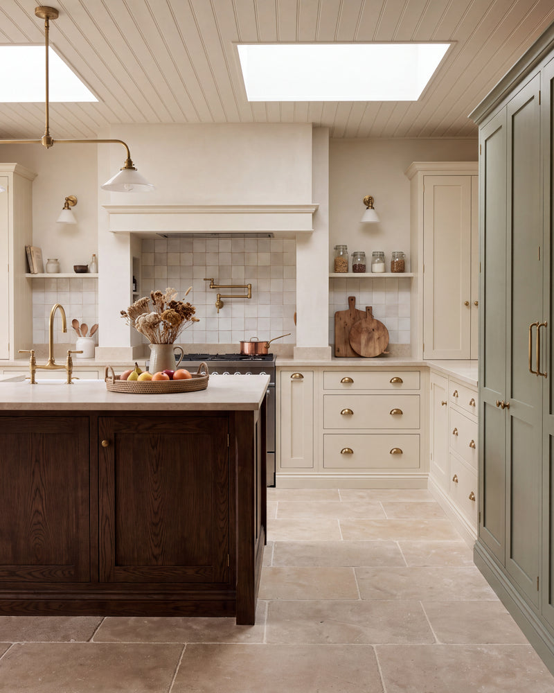 Riviera Limestone Tumbled flagstones running across a country kitchen floor, with a dark oak island, cream shaker cabinetry and a sage green larder cupboard