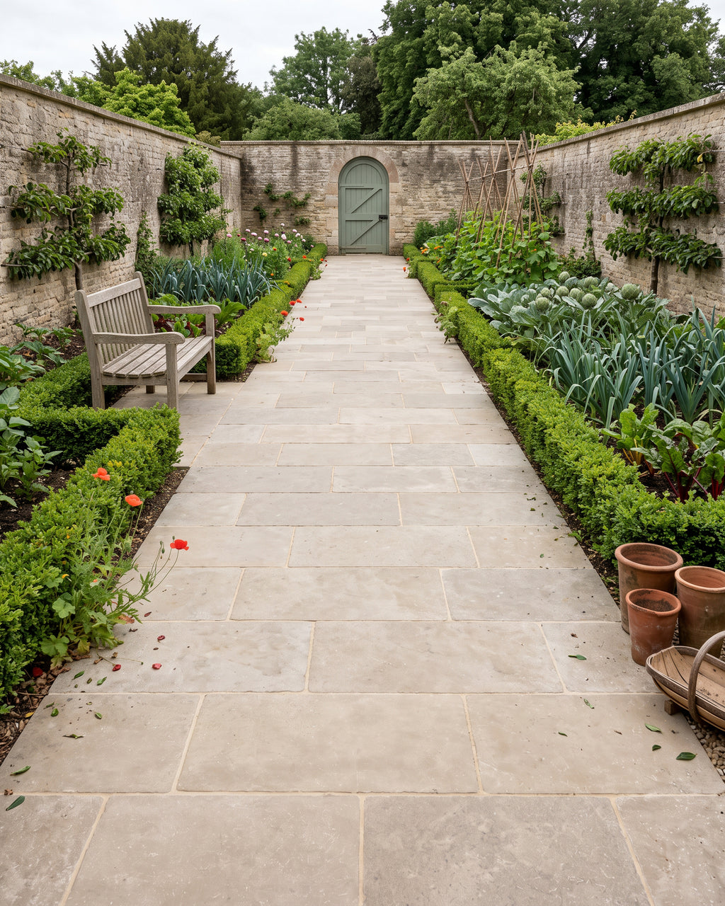 Riviera Limestone Tumbled paving laid as a wide path down a walled kitchen garden, box-edged beds of leeks, chard and artichokes either side and a sage green door in the far wall