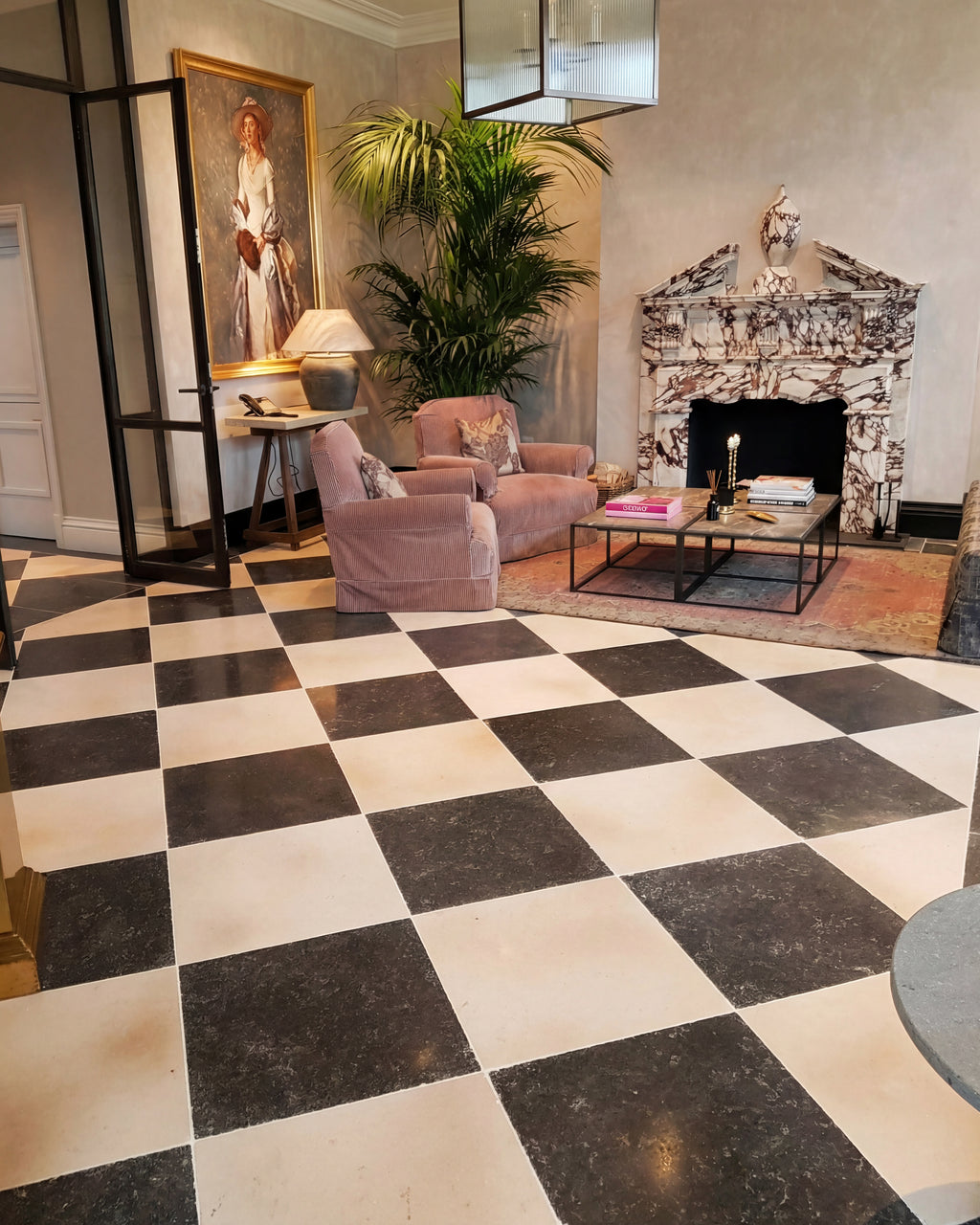 Royal Mink Limestone Tumbled Finish laid as a large chequerboard with a cream limestone across a drawing room with a Calacatta Viola fireplace and pink velvet armchairs