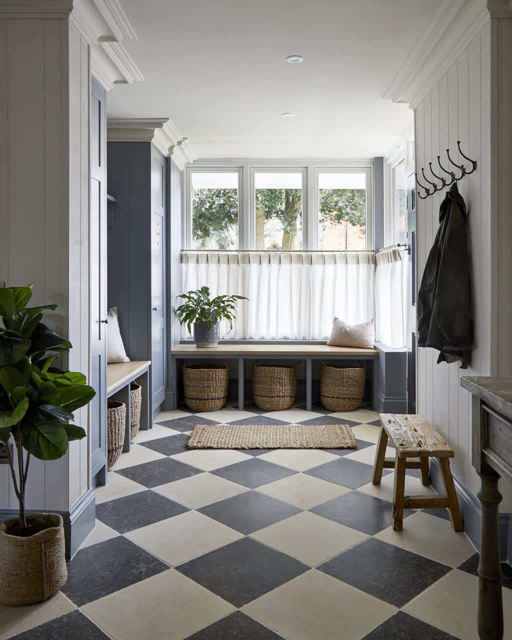 Royal Mink Limestone Tumbled Finish in a diagonal chequerboard with Mallory Limestone across a panelled boot room with a window seat and basket storage