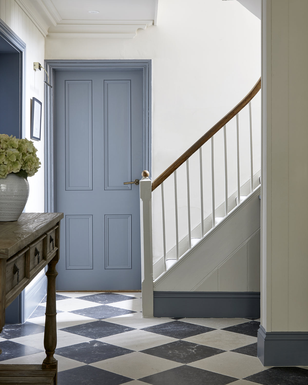 Royal Mink Limestone Tumbled Finish in a chequerboard with Mallory Limestone in a hallway with a blue panelled door, oak console and painted staircase