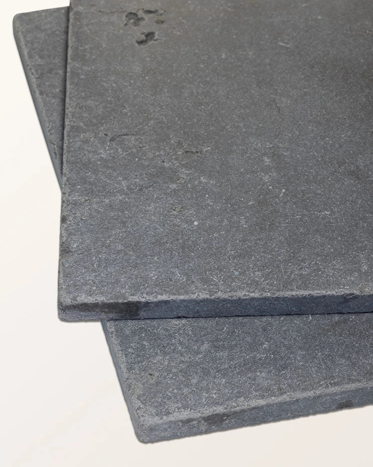 Two Royal Mink Limestone Tumbled Finish tiles stacked at an angle against a plain background, showing the dark grey surface and tumbled edge