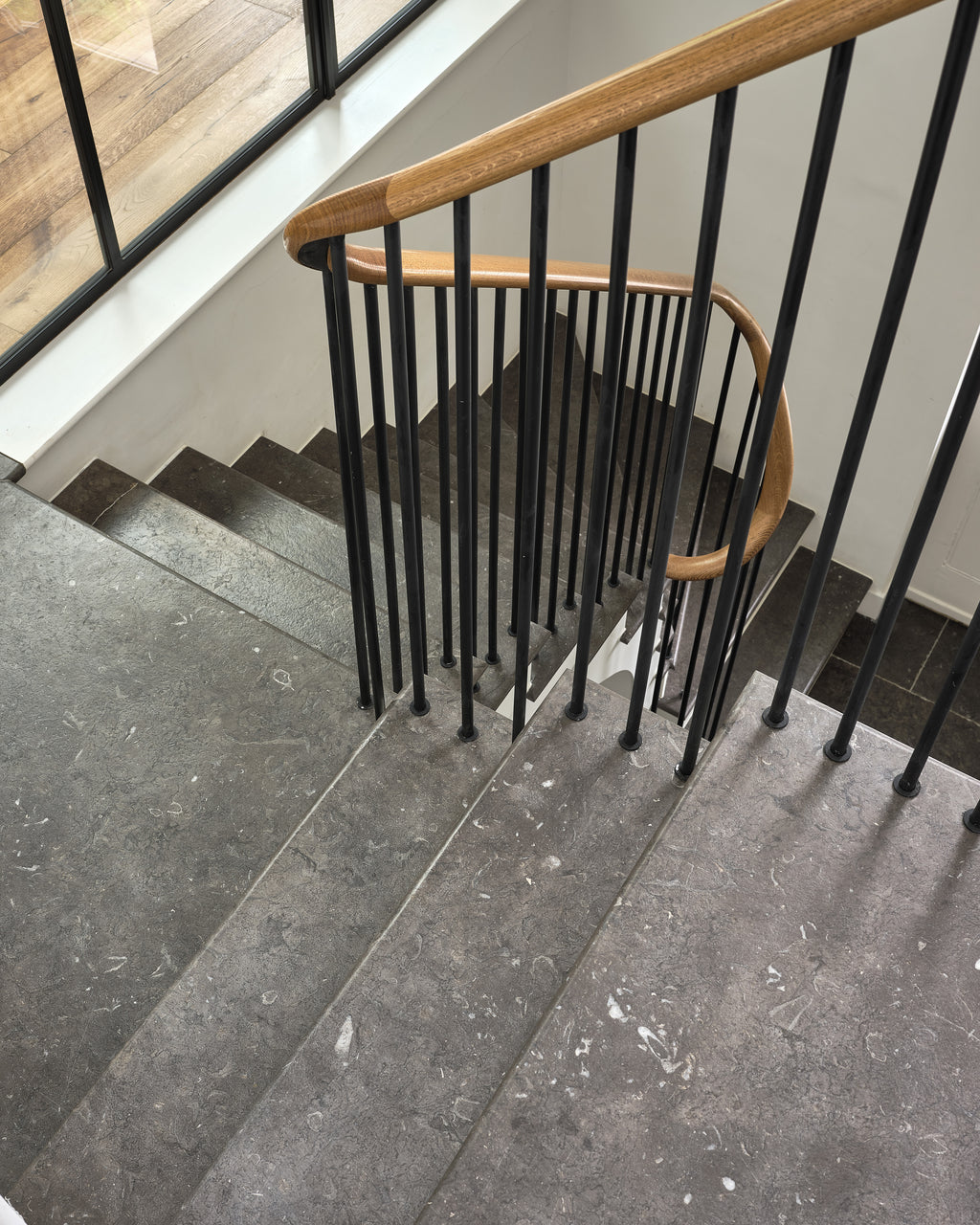 Royal Mink Limestone Tumbled Finish stair treads seen from above, curving past a black spindle balustrade and an oak handrail