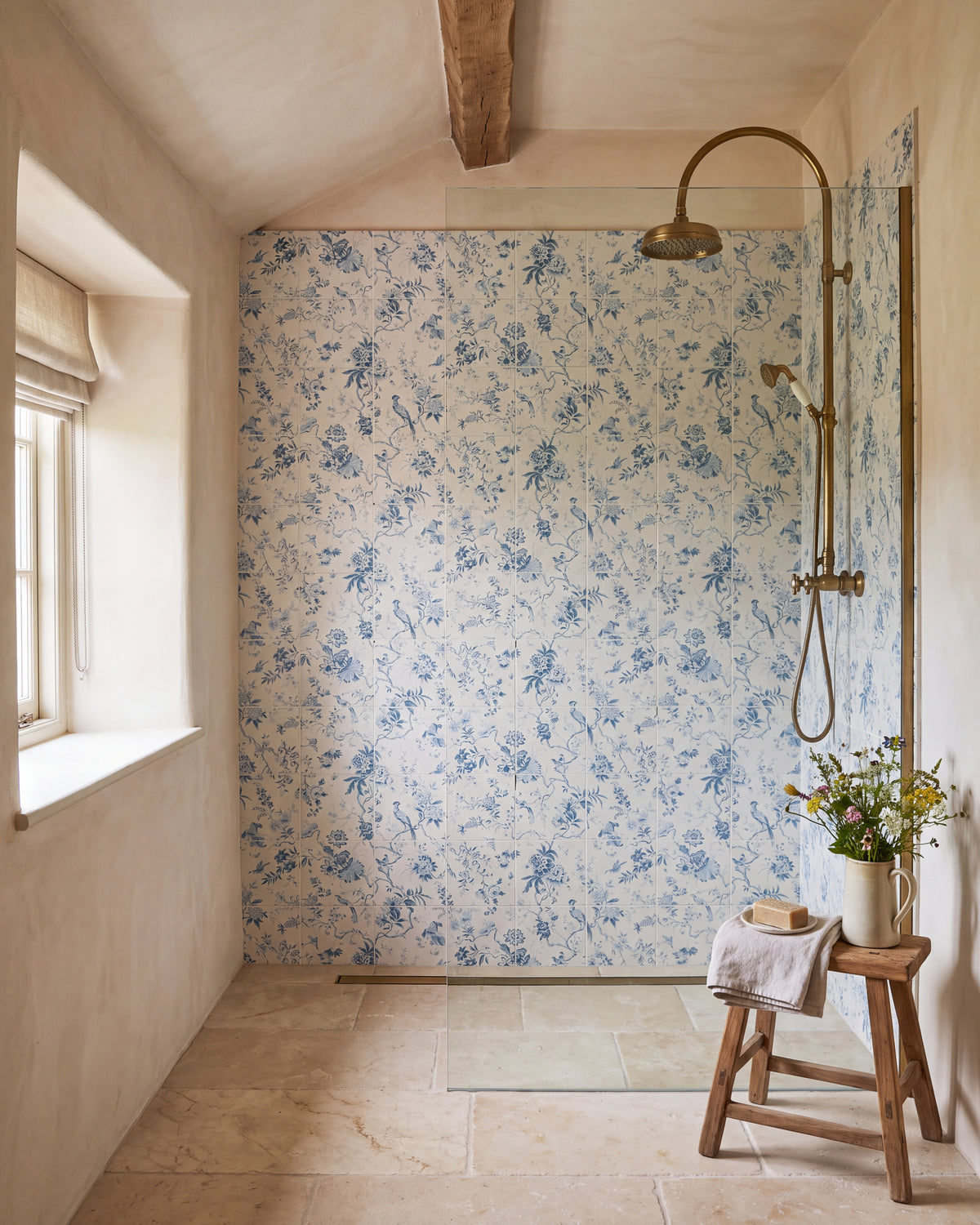 Sanderson Pillemont Toile China Blue Mural Porcelain lining a walk-in shower in a beamed cottage bathroom, with an aged brass rainfall shower and a limestone floor