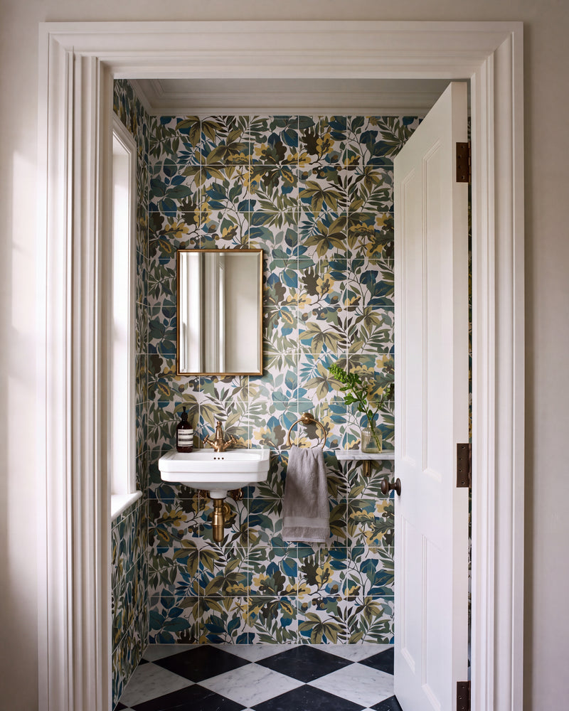 Sanderson Robin's Wood Sage Pattern lining a cloakroom seen through an open panelled door, with a wall-hung basin, brass tap and towel ring, a gilt mirror and a black and white marble chequerboard floor