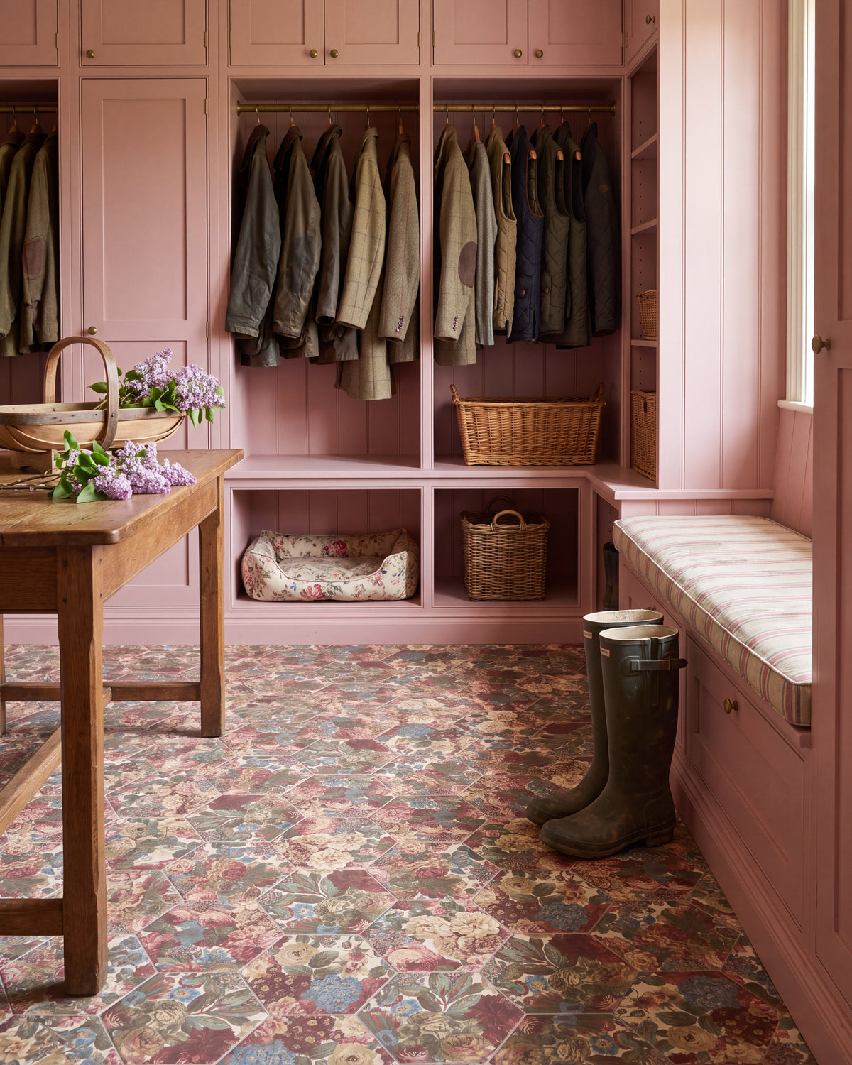 Sanderson Very Rose & Peony Madder Porcelain hexagons underfoot in a pink-painted boot room, with hanging tweed and waxed jackets, wicker baskets, a striped window seat and a floral dog bed