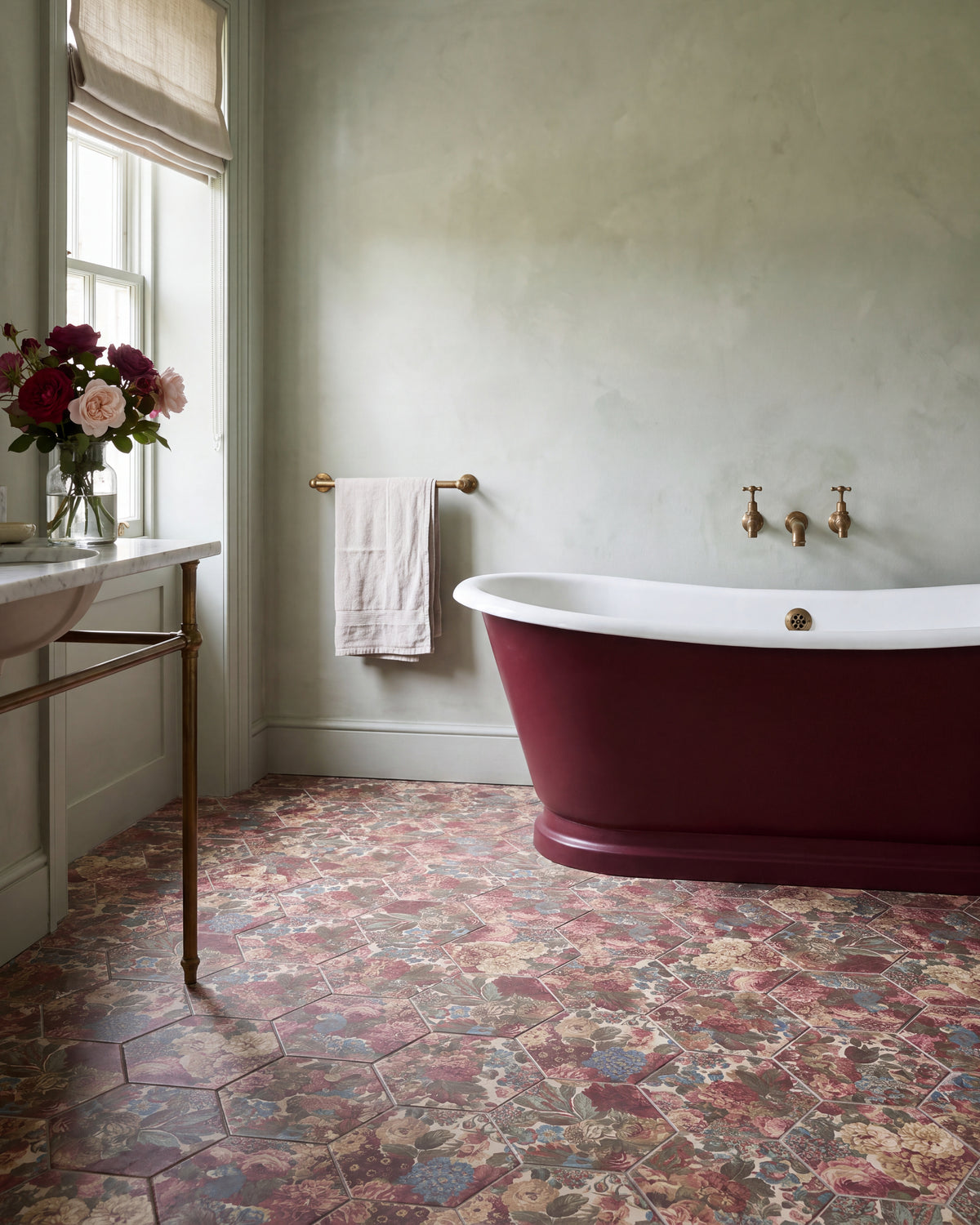 Sanderson Very Rose & Peony Madder Porcelain hexagons across a calm bathroom floor, with a burgundy roll-top bath, wall-mounted brass taps, a marble washstand and garden roses at the window